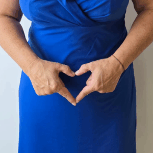 Vrouw in blauwe jurk vormt een hart met haar handen over haar buik als symbool voor darmgezondheid en innerlijke rust.